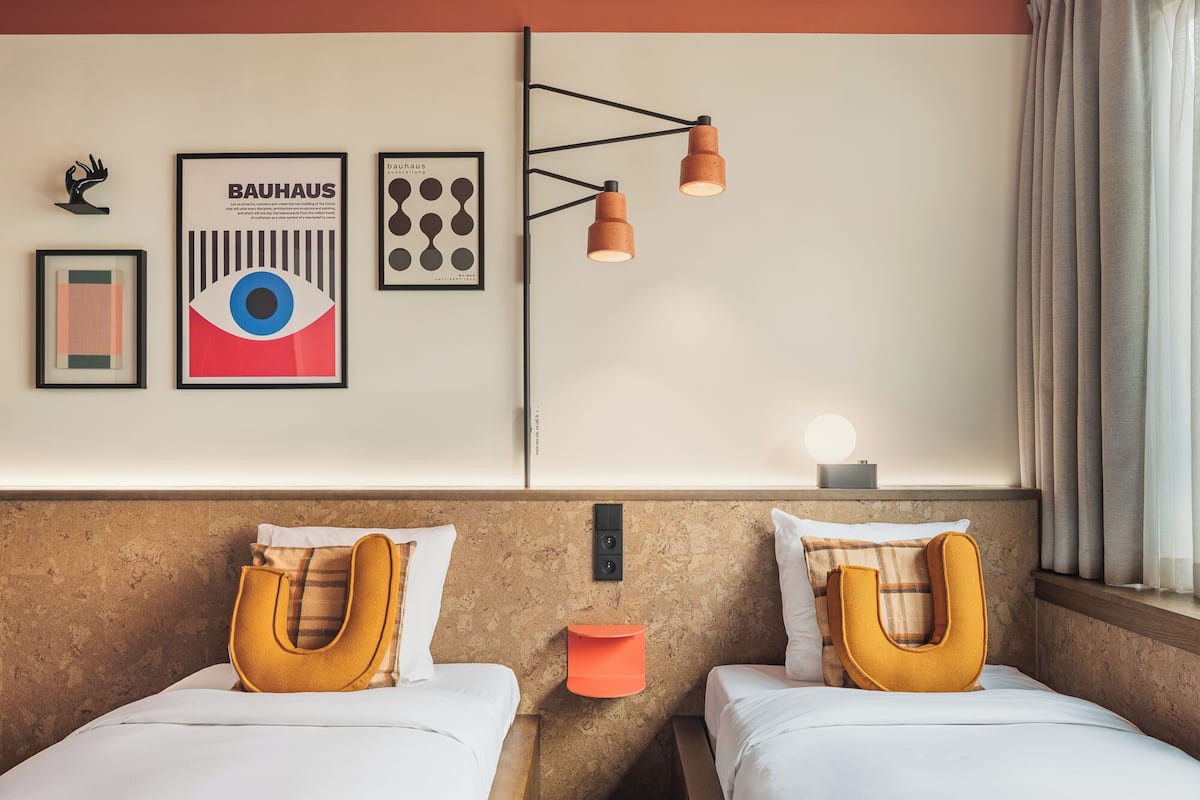 A hotel room with two beds, a wall-mounted light fixture, and framed artwork.