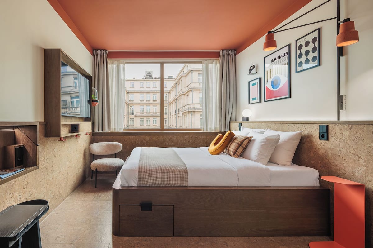 A modern hotel room with a large bed, a desk, a chair, and a window with a city view.