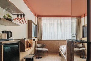 Una habitación de hotel moderna con un ventanal grande, un televisor de pantalla plana, un escritorio con una silla, una cama y una pequeña mesa con una silla.