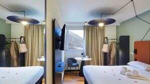 Ein Hotelzimmer mit zwei Betten, einem Schreibtisch, einem Stuhl, einem Fernseher und einem Fenster mit Vorhängen.
