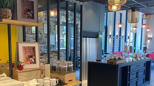 Ein modernes Café-Interieur mit Holztisch, bewehrten Speisekarten und einer zentralen Theke mit Gläsern.