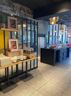 Un café moderno con una mesa de madera, carteles de menú enmarcados y una isla central con frascos.
