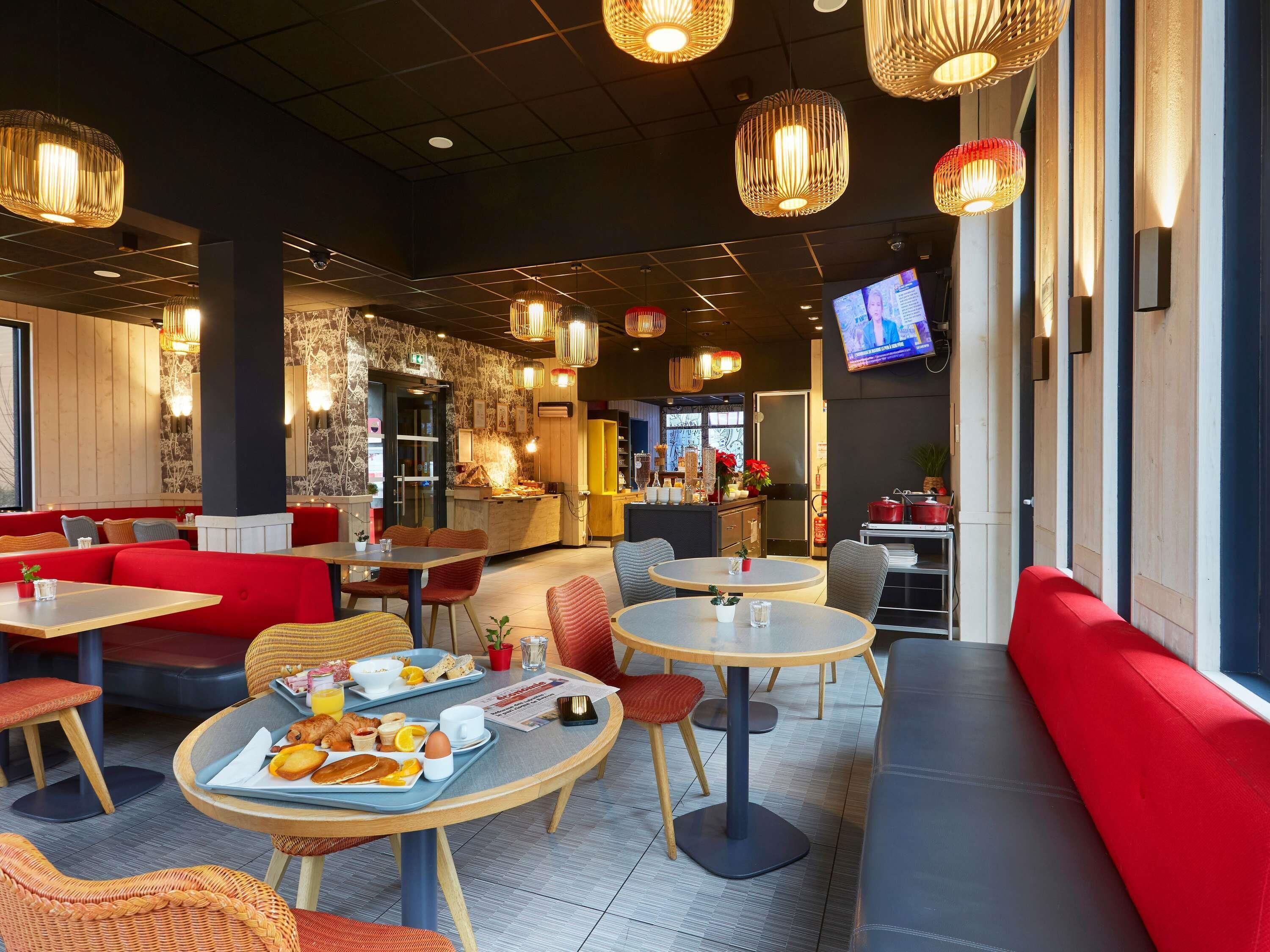 A modern dining area with round tables, red seating, and decorative hanging lights.