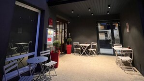 Ein Außenbereich mit Tischen und Stühlen, ein rotes Schild für ibis Hotels und ein Hauseingang.