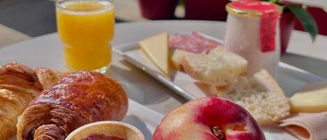 Bandeja de desayuno con cruasanes, un melocotón, una tartaleta pequeña, queso, pan y un vaso de zumo de naranja.