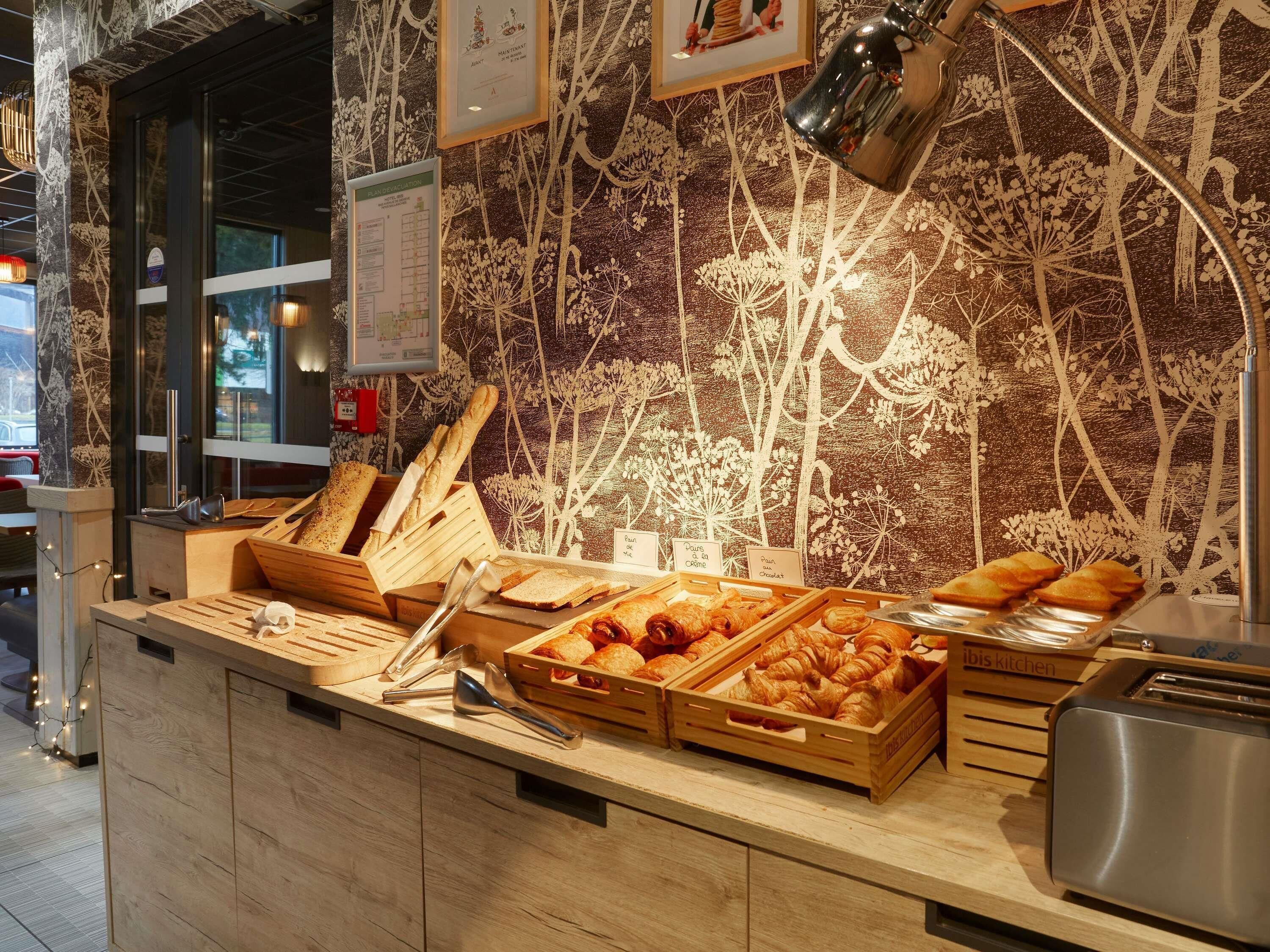 Un mostrador de panadería con diversos productos horneados, un cartel con el menú y una zona de cocina.