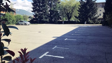 Parcheggio con posti delimitati, circondato da alberi e edifici.