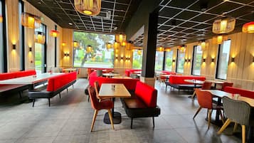 A restaurant with booths and tables, large windows, and hanging pendant lights.