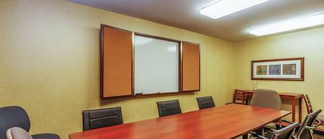 Ein Konferenzraum mit einem langen Holztisch, sechs Stühlen, einer Whiteboard-Tafel und einem gerahmten Bild an der Wand.