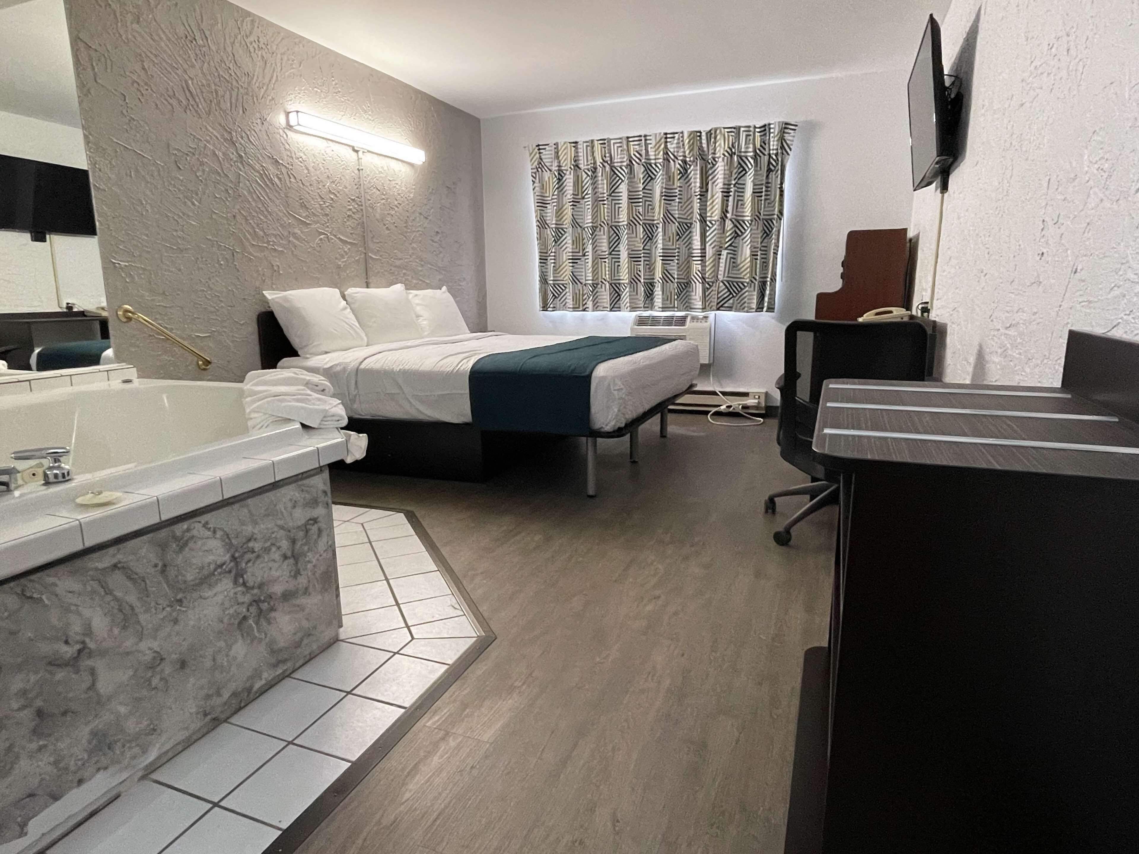 Une chambre d’hôtel moderne dotée d’un grand lit, d’un coin salon séparé, d’une salle de bain avec baignoire et d’un bureau avec une chaise.