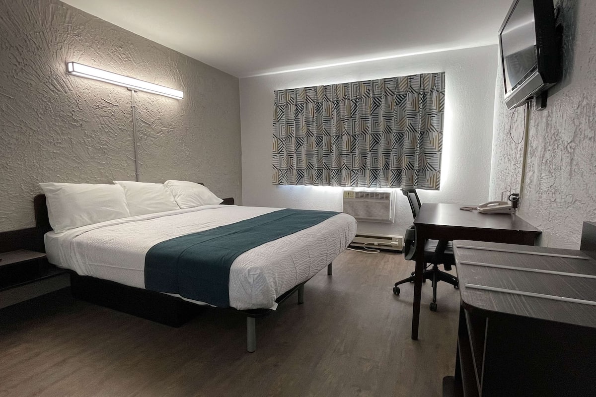 A modern hotel room with a large bed, a desk, and a television.