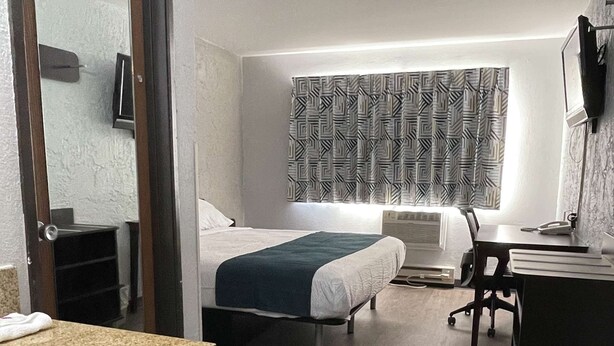 A hotel room with two beds, a desk, a chair, a desk lamp, a mirror, and a bathroom with a sink and toilet.