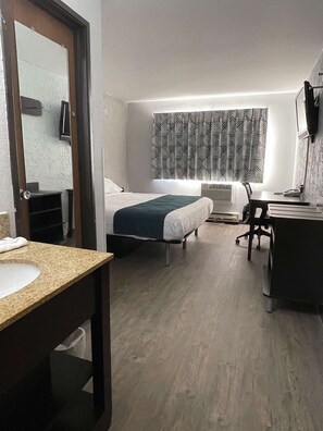 A hotel room with two beds, a desk, a chair, a desk lamp, a mirror, and a bathroom with a sink and toilet. - Motel 6 Green Bay, WI - Lambeau (Green Bay)