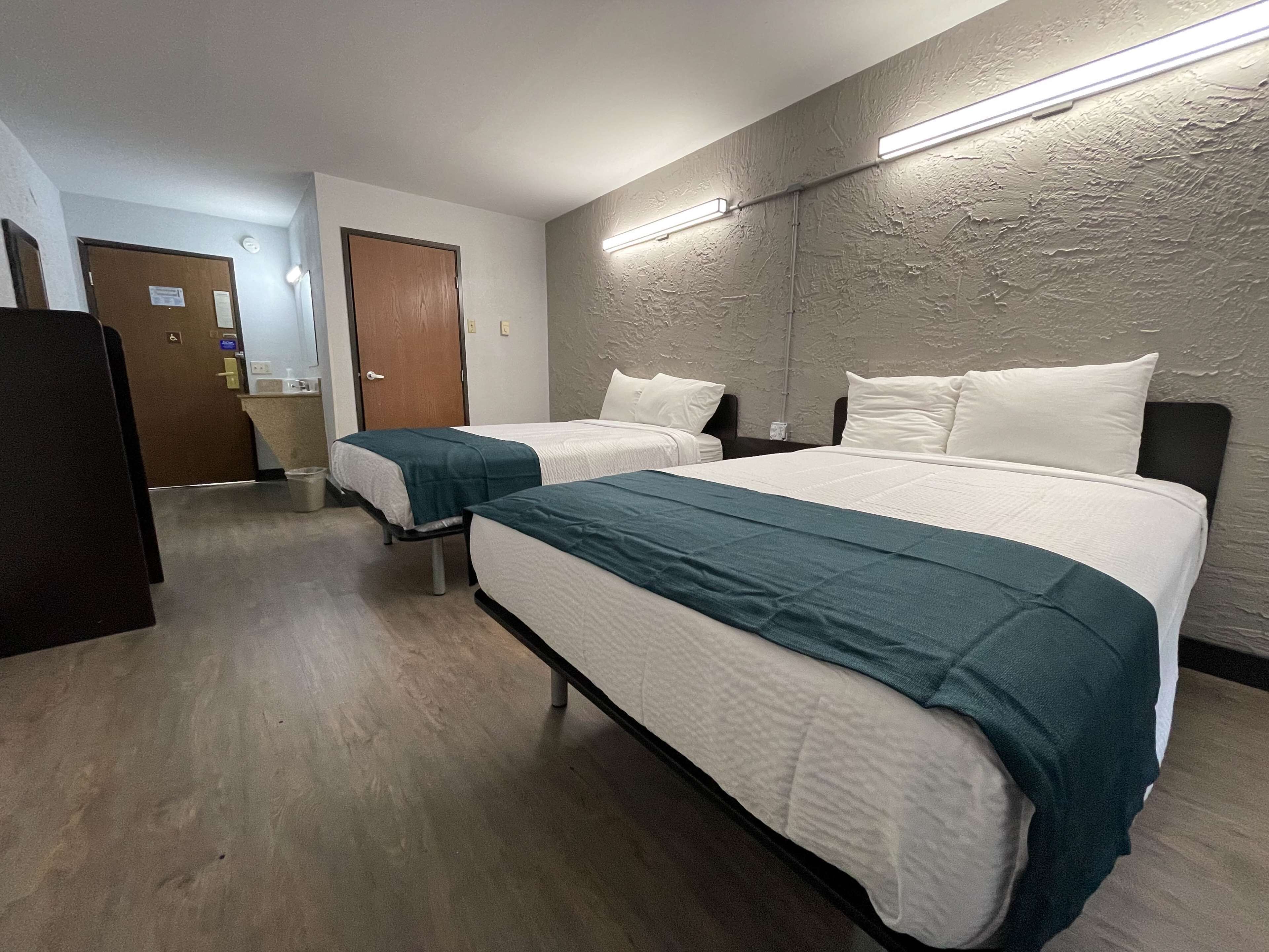 A hotel room with two beds, wooden flooring, a large mirror, and a door leading to a bathroom.