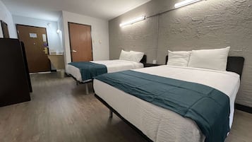 Habitación de hotel con dos camas, suelo de madera, un espejo grande y una puerta que da al baño.