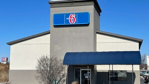 A motel with a prominent '6' sign on the facade, a covered entrance, and a parking lot visible in the background.
