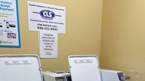 A laundromat with two front-loading washing machines and a dryer. There are signs indicating the laundromat is owned by CLS and provides commercial laundry services.