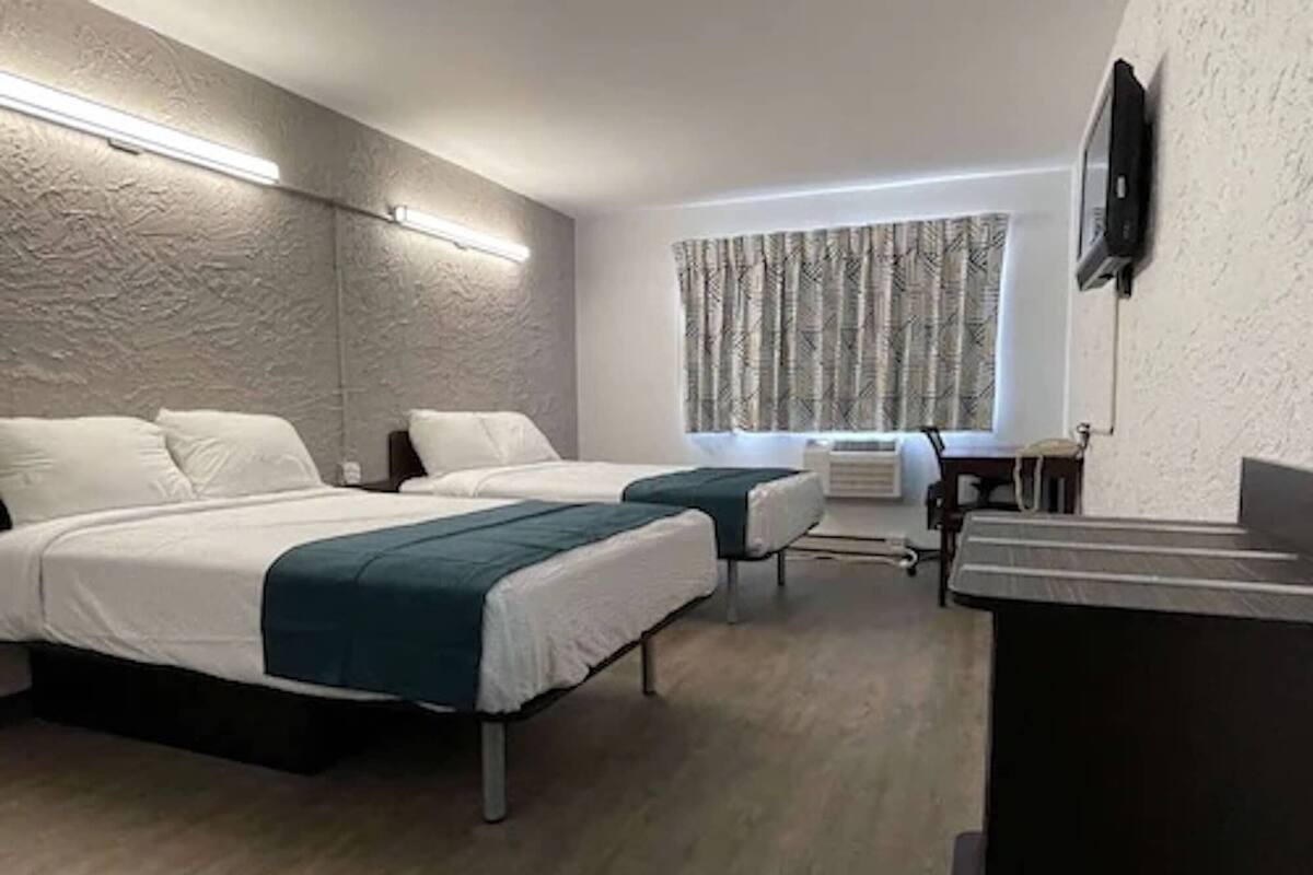 A hotel room with two beds, a desk, a chair, a flat-screen TV, and a window with curtains.