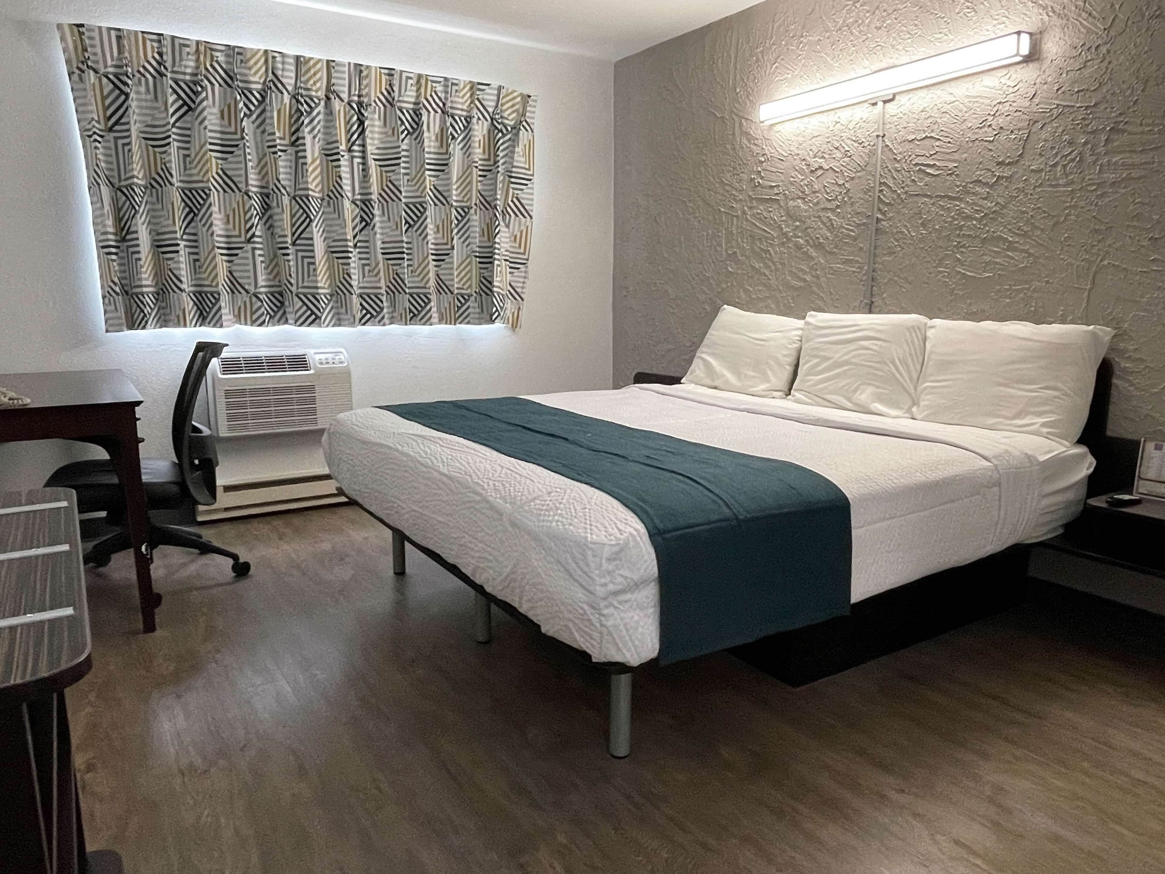 A modern hotel room with a bed, a desk, a chair, and a wall-mounted air conditioner.