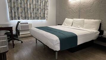 A modern hotel room with a bed, a desk, a chair, and a wall-mounted air conditioner.