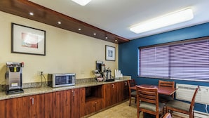 A kitchenette with a microwave, coffee maker, and a small refrigerator. There is a dining area with a table and chairs, and a window with blinds.