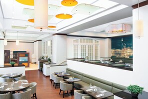 A modern restaurant with high ceilings, pendant lighting, and a cityscape view.