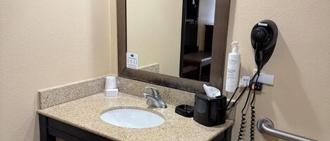 A bathroom with a sink, mirror, hairdryer, and toilet.