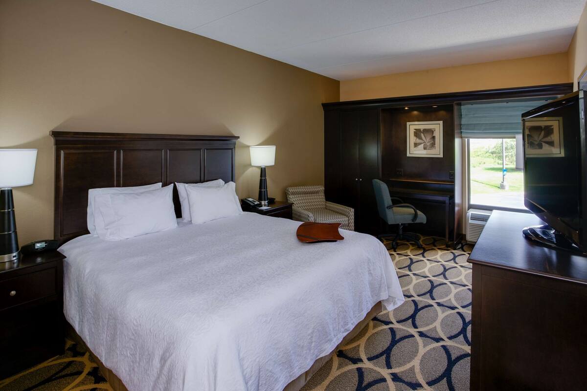 A hotel room with a large bed, a desk, a chair, and a view of the outdoors.
