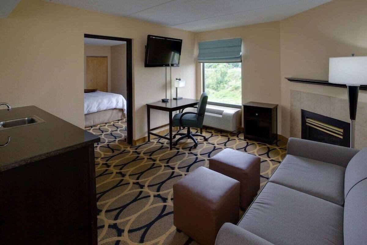 A hotel room with a bed, a desk with a TV, a sofa, a fireplace, and a patterned carpet.
