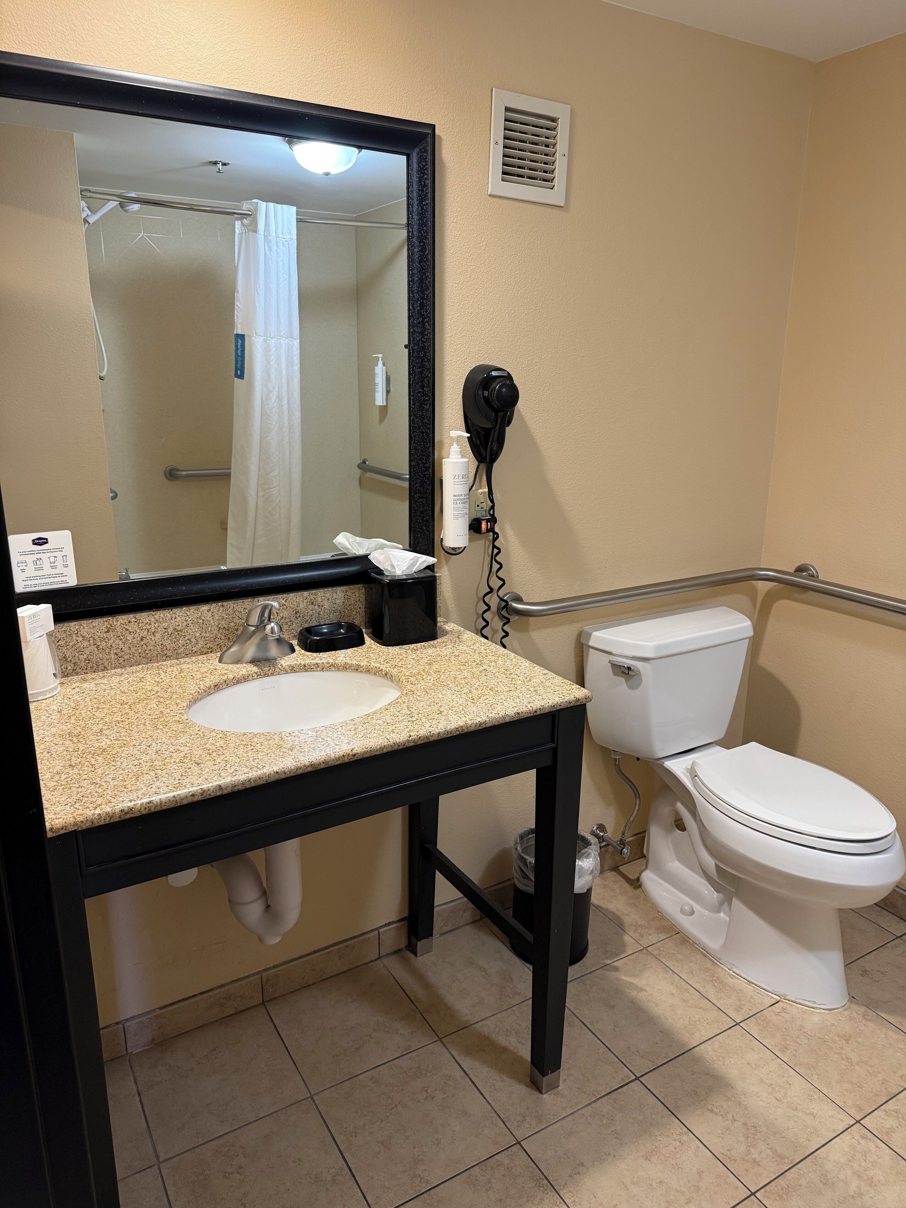 Ein Badezimmer mit Waschbecken, Spiegel, Toilette und einem an der Wand befestigten Fön.