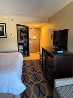 Habitación de hotel con cama, escritorio con televisor, microondas y baño visible a través de una puerta abierta.