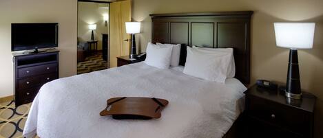 A hotel room with a large bed, a flat-screen TV, a bedside table with a lamp, and a nightstand with a lamp.