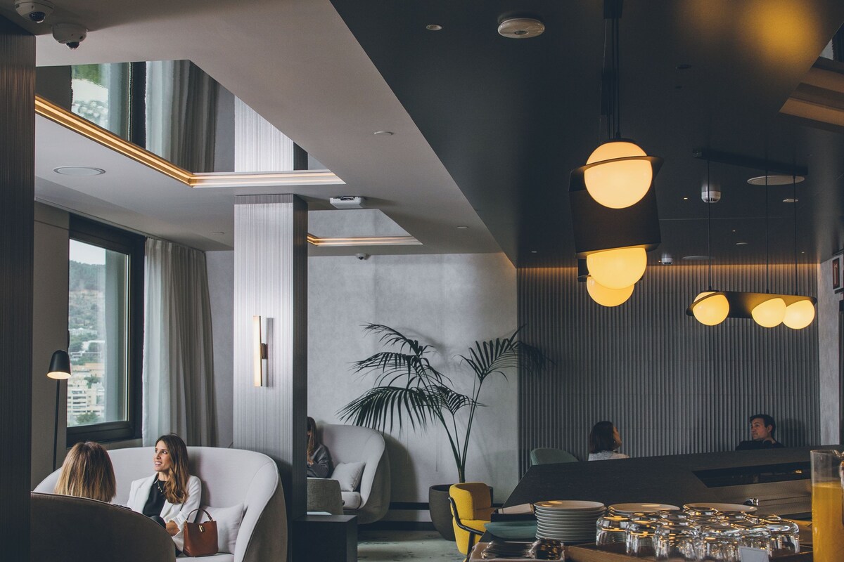 A modern hotel lobby with a reception desk, seating area, and large windows.