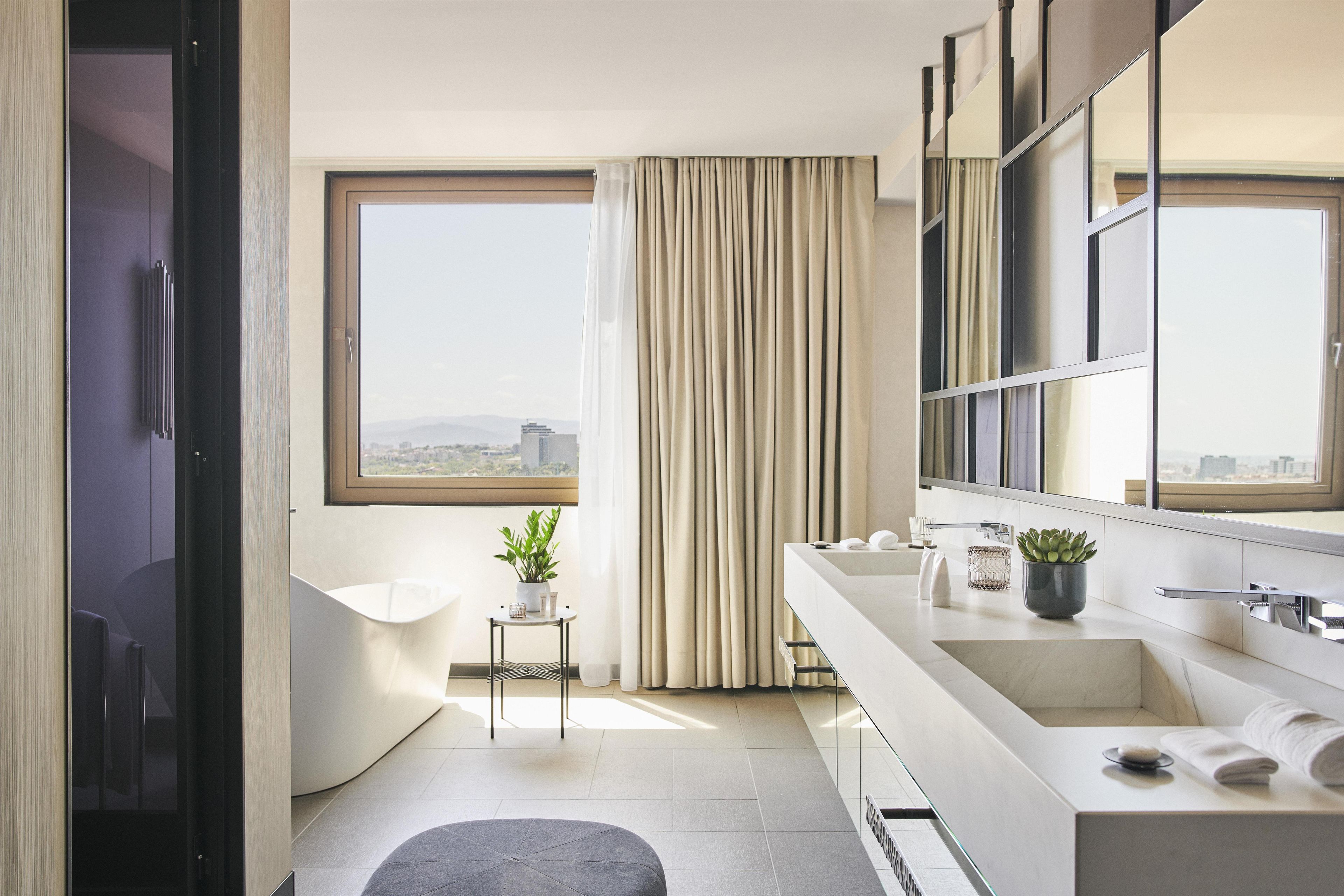 A modern bathroom with a large window, a bathtub, a sink, and a mirror.
