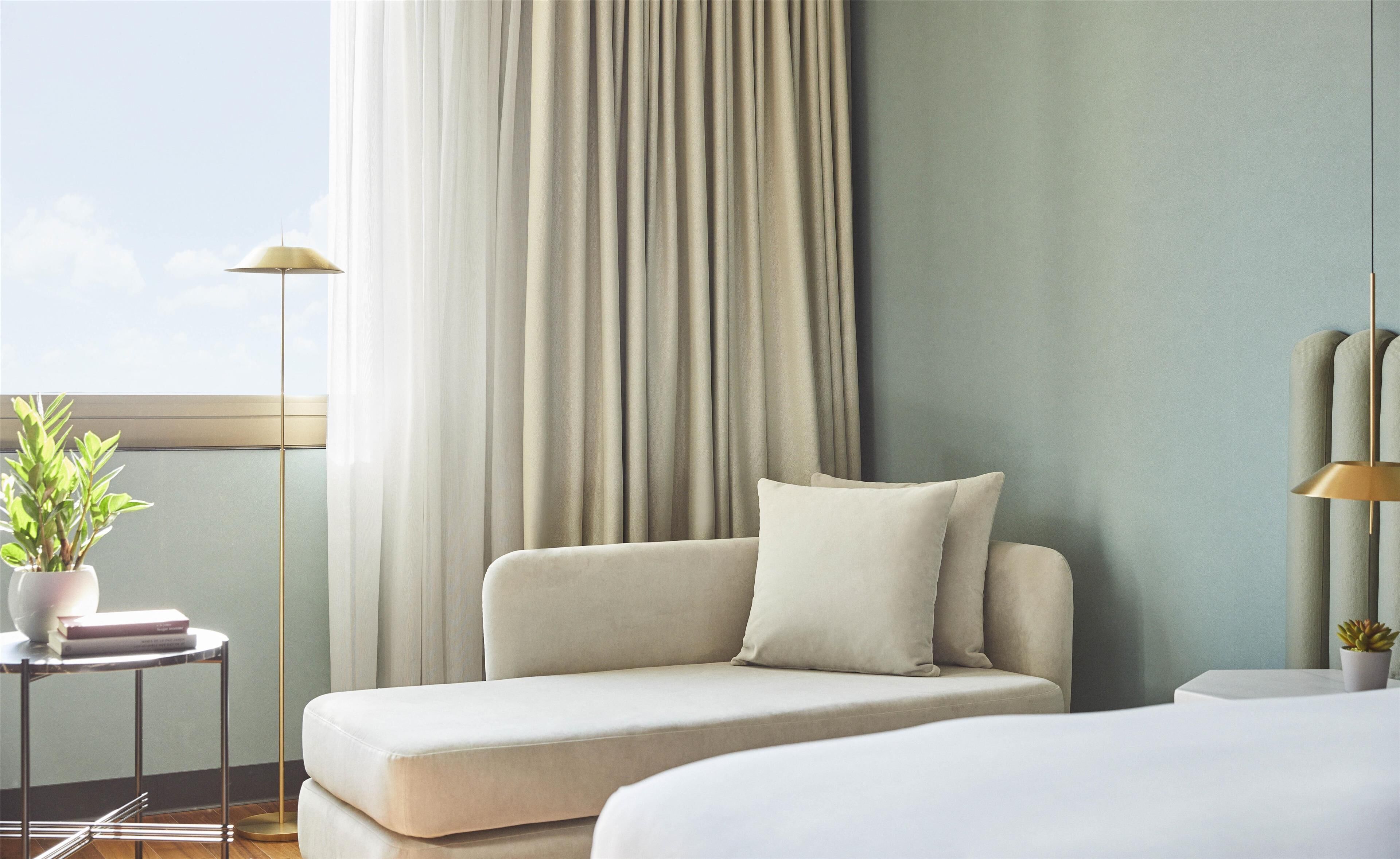 A modern hotel room with a sofa, a small table with a plant, and a lamp.