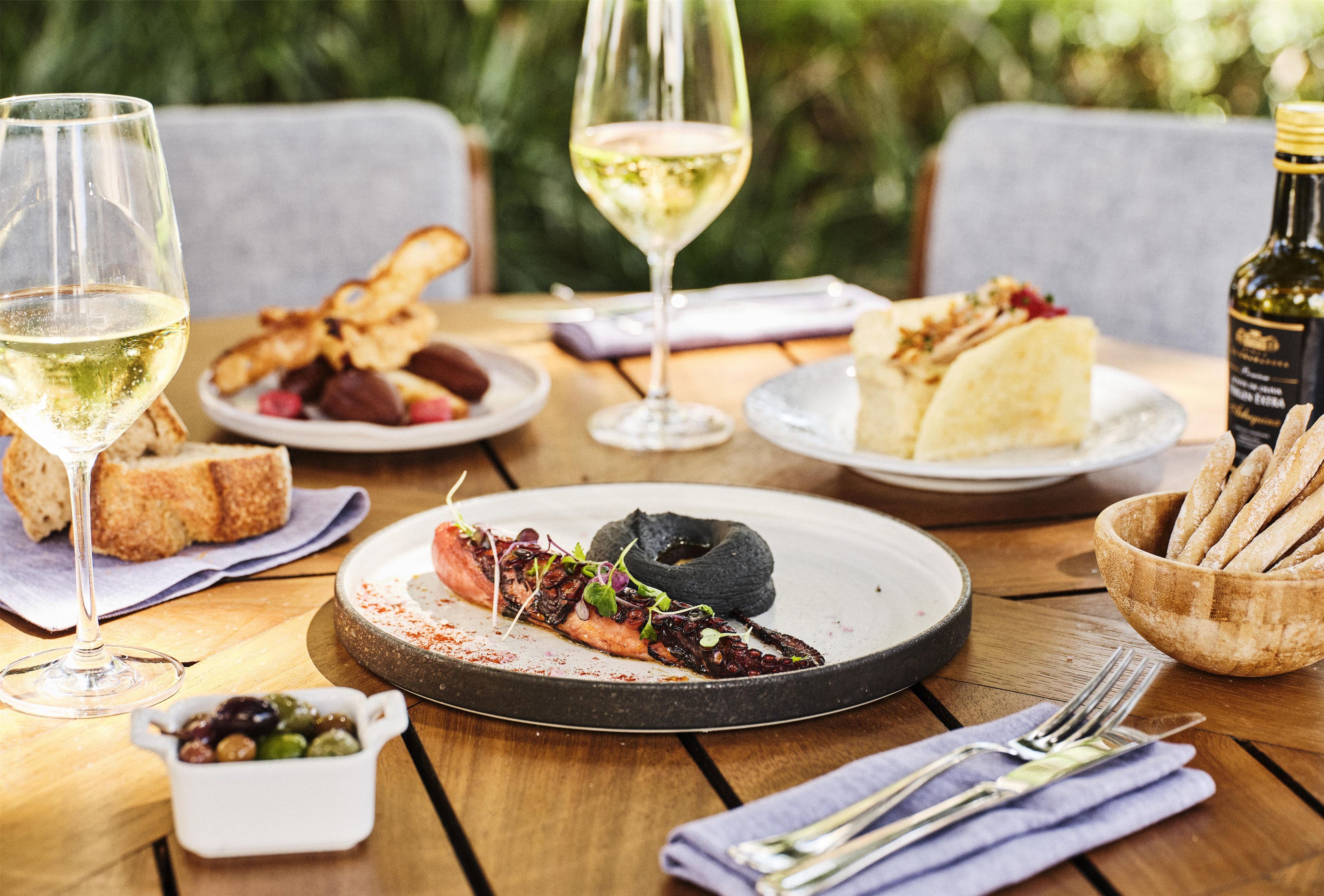 A dining table with plates of food, glasses of wine, and a bottle of wine.