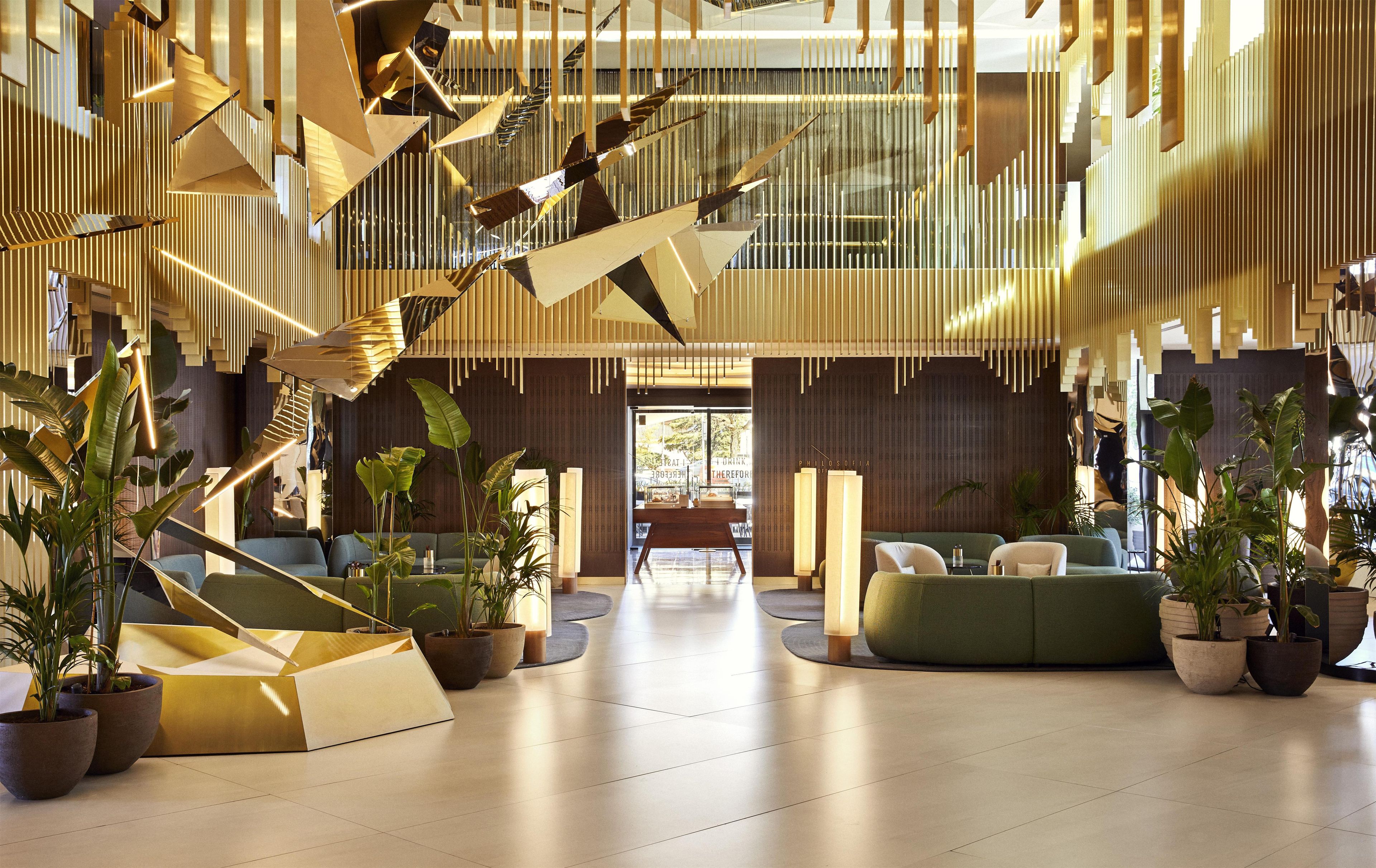A modern lobby with a geometric ceiling design, seating areas, and potted plants.