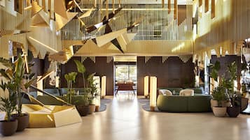 A modern lobby with a geometric ceiling design, seating areas, and potted plants.