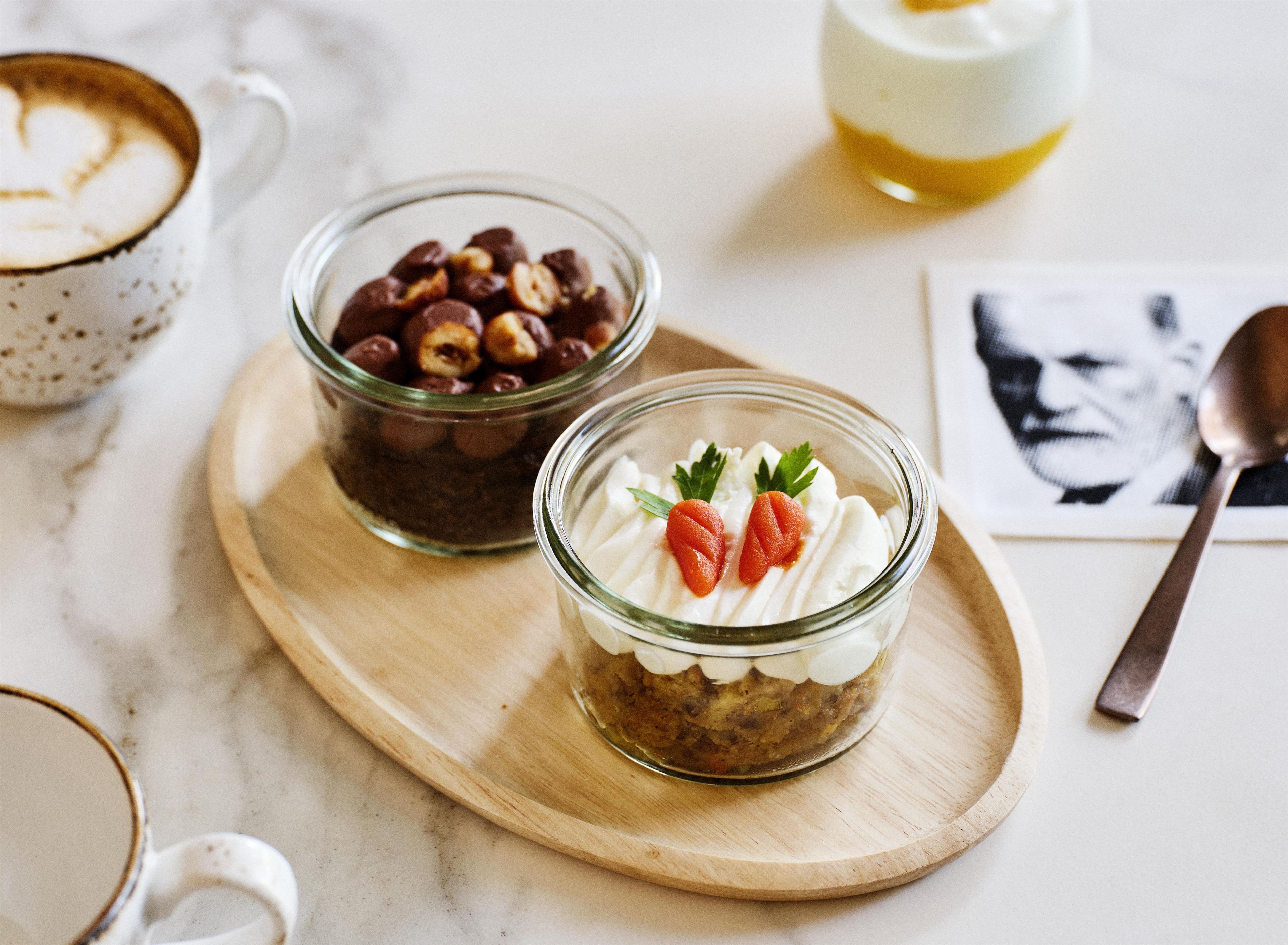 Uma tábua de madeira com duas tigelas de vidro contendo alimentos, uma colher e uma caneca com bebida.
