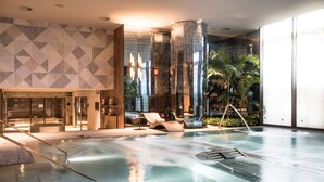 Un área de piscina interior moderna con un diseño geométrico en la pared, un mostrador de recepción y asientos tipo lounge.