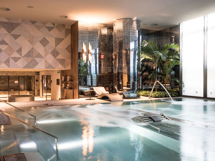 Un área de piscina interior moderna con un diseño geométrico en la pared, un mostrador de recepción y asientos tipo lounge.