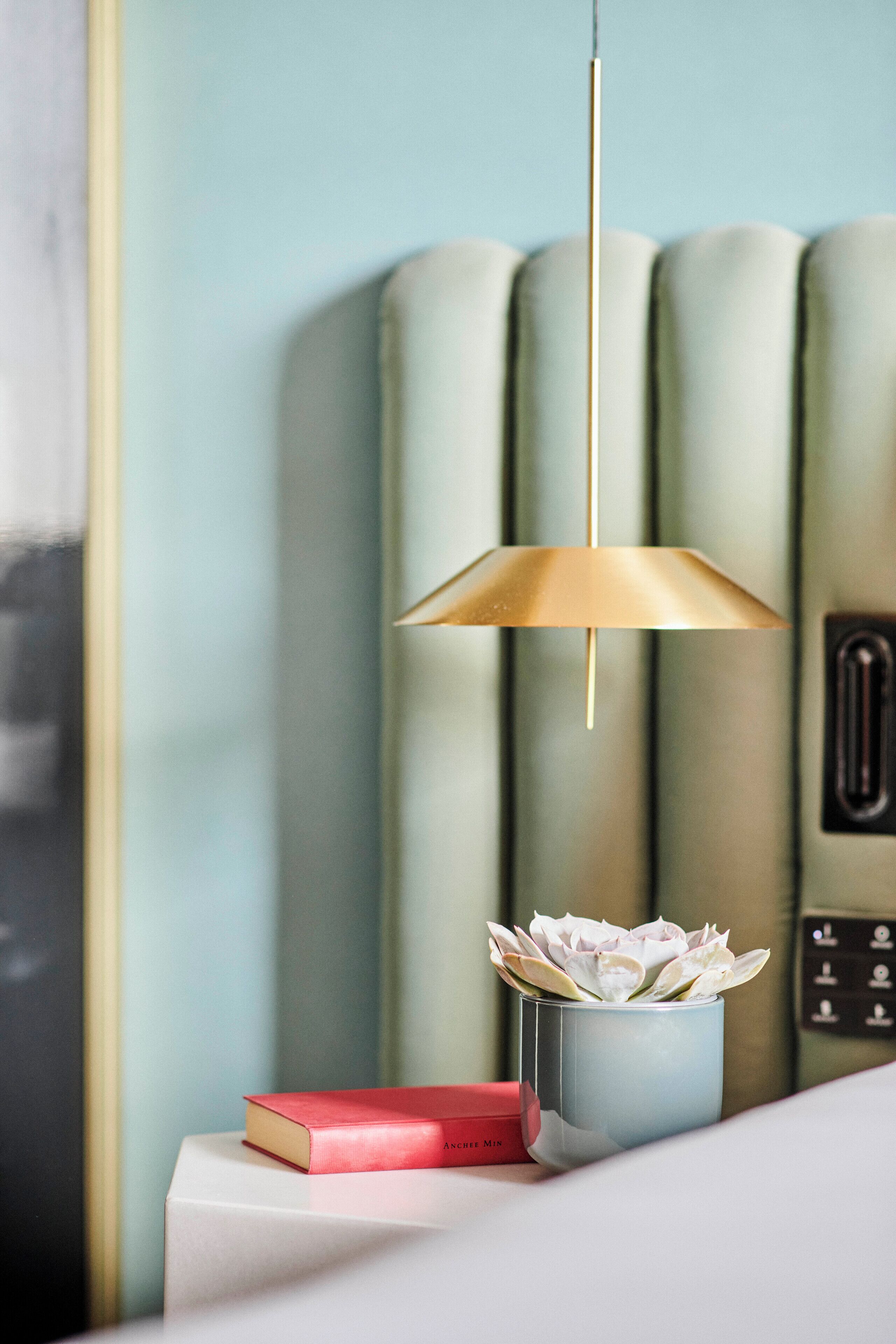 A modern room with a minimalist design, featuring a white bedside table, a blue vase with white flowers, and a red book.