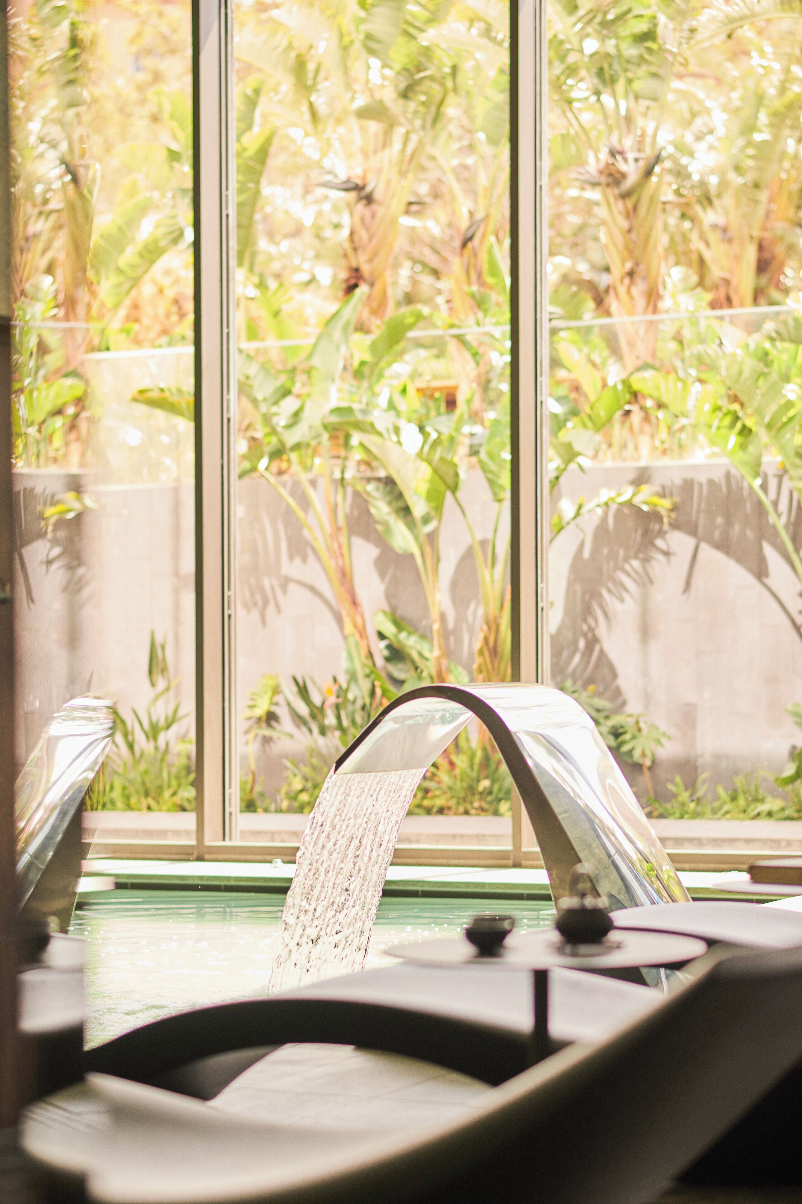 A spa area with a water feature and a view of lush greenery through large windows.