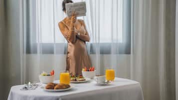 En frukostuppdukning med ett bord för två personer, inklusive croissanter, frukt och juice.