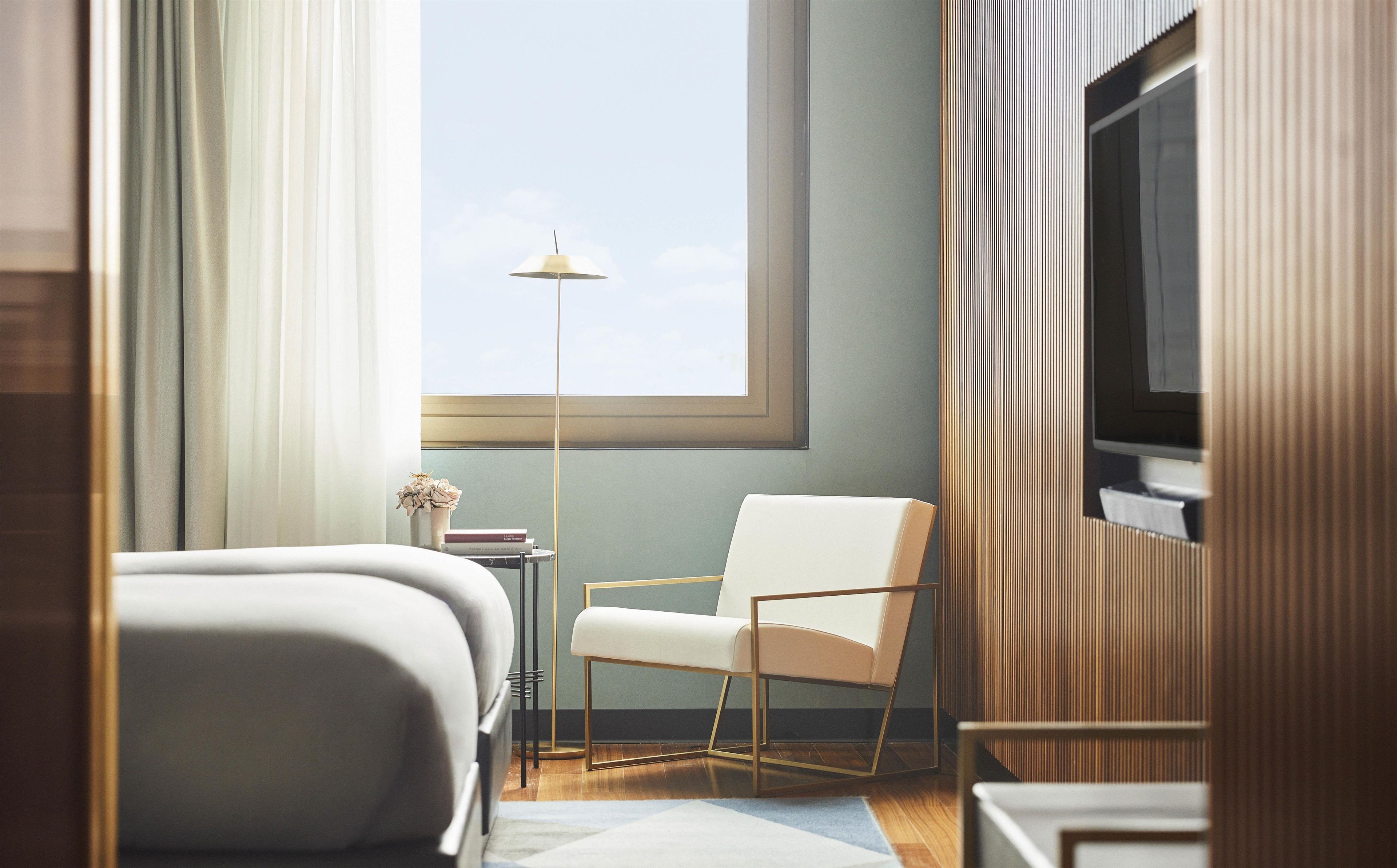 A hotel room with a bed, a chair, a floor lamp, a television, and a window with a view.