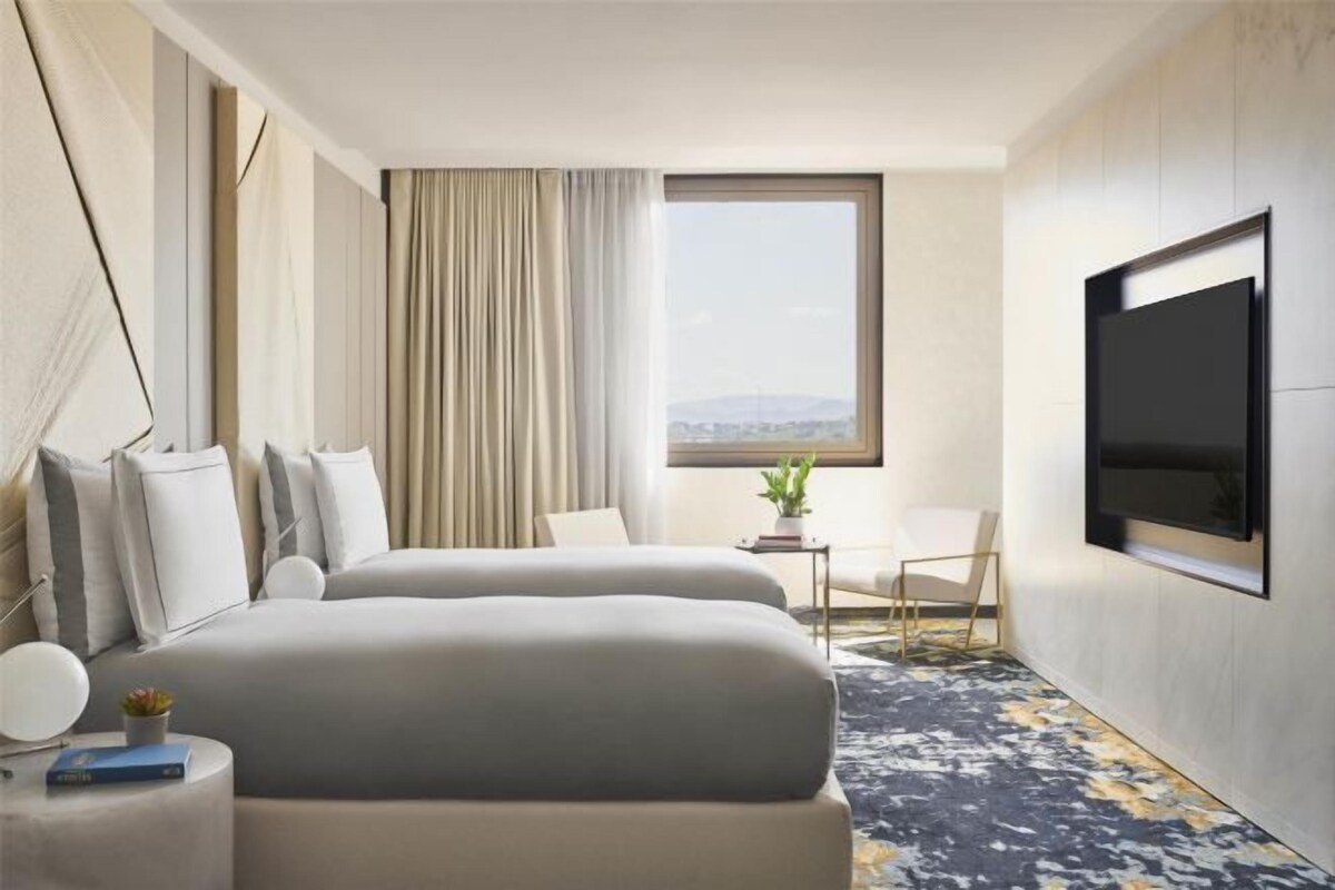 A hotel room with a bed, a TV, a desk, and a window with a view.