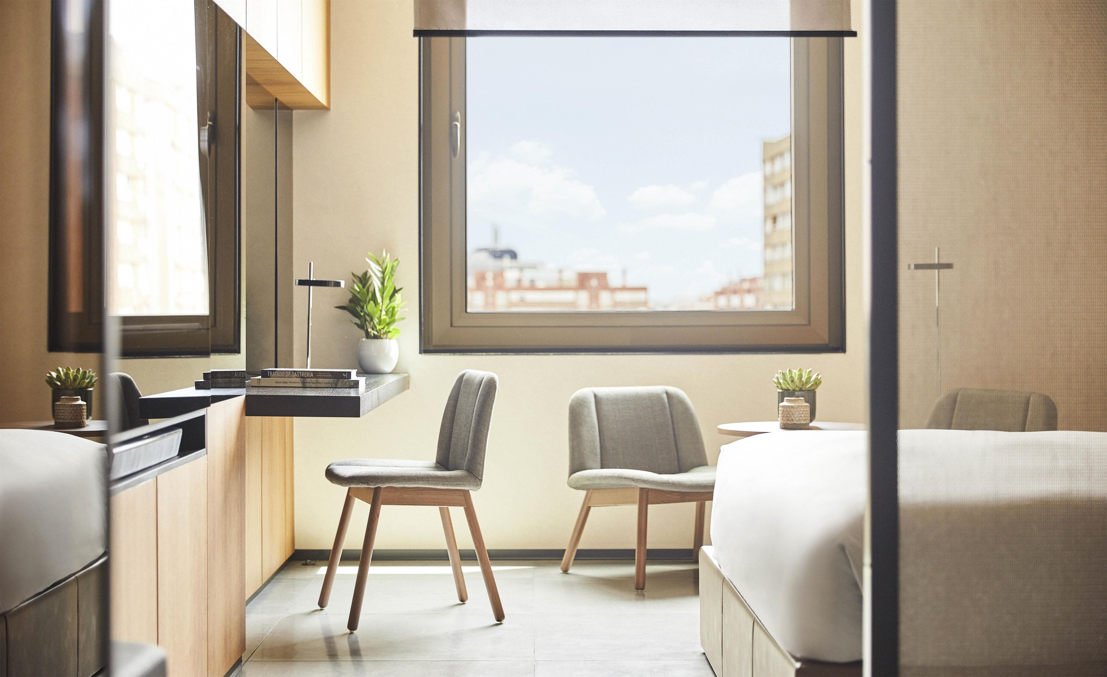 A modern bedroom with a large window, a bedside table with a plant, and a chair.