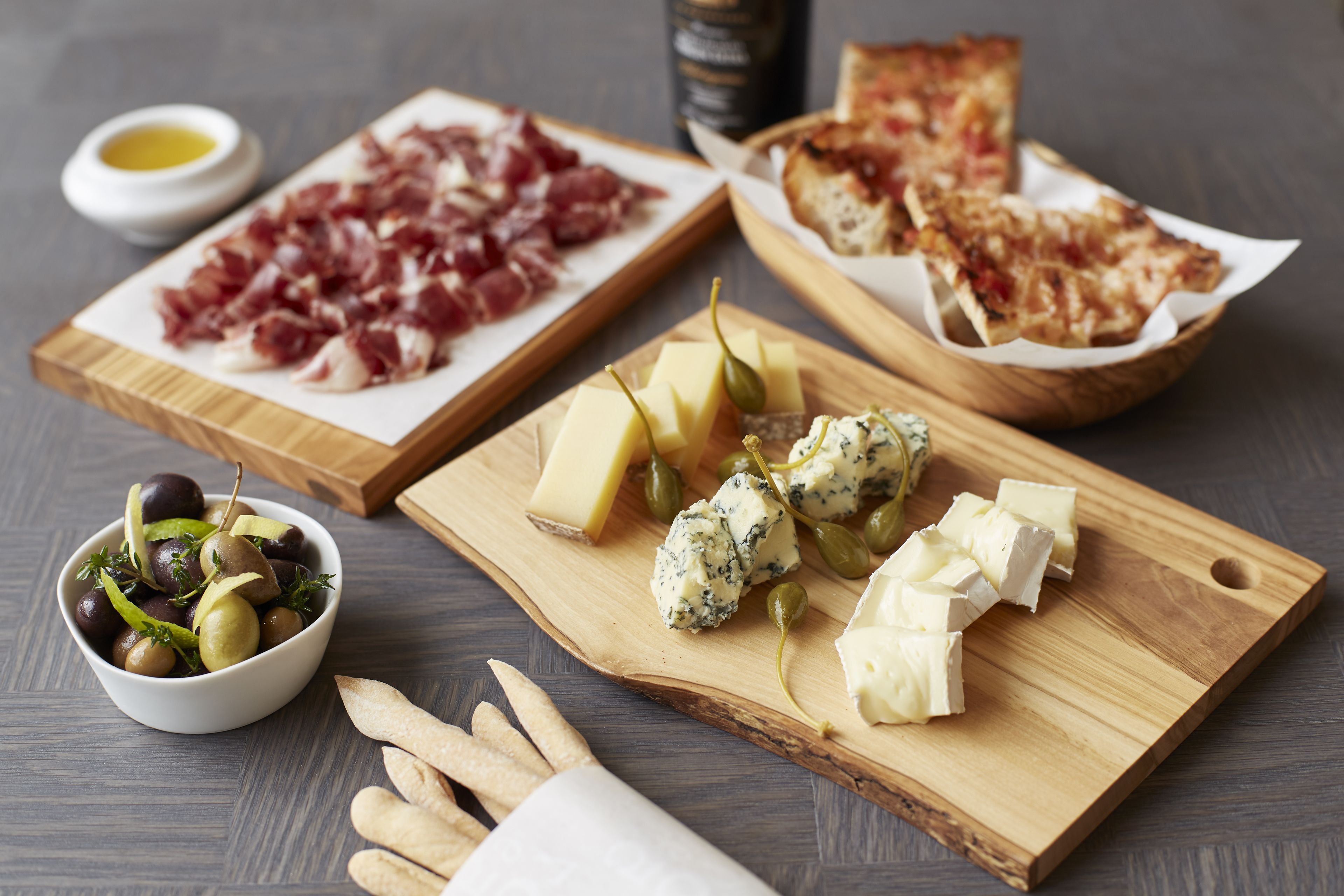 A wooden board with various cheeses, olives, and crackers.