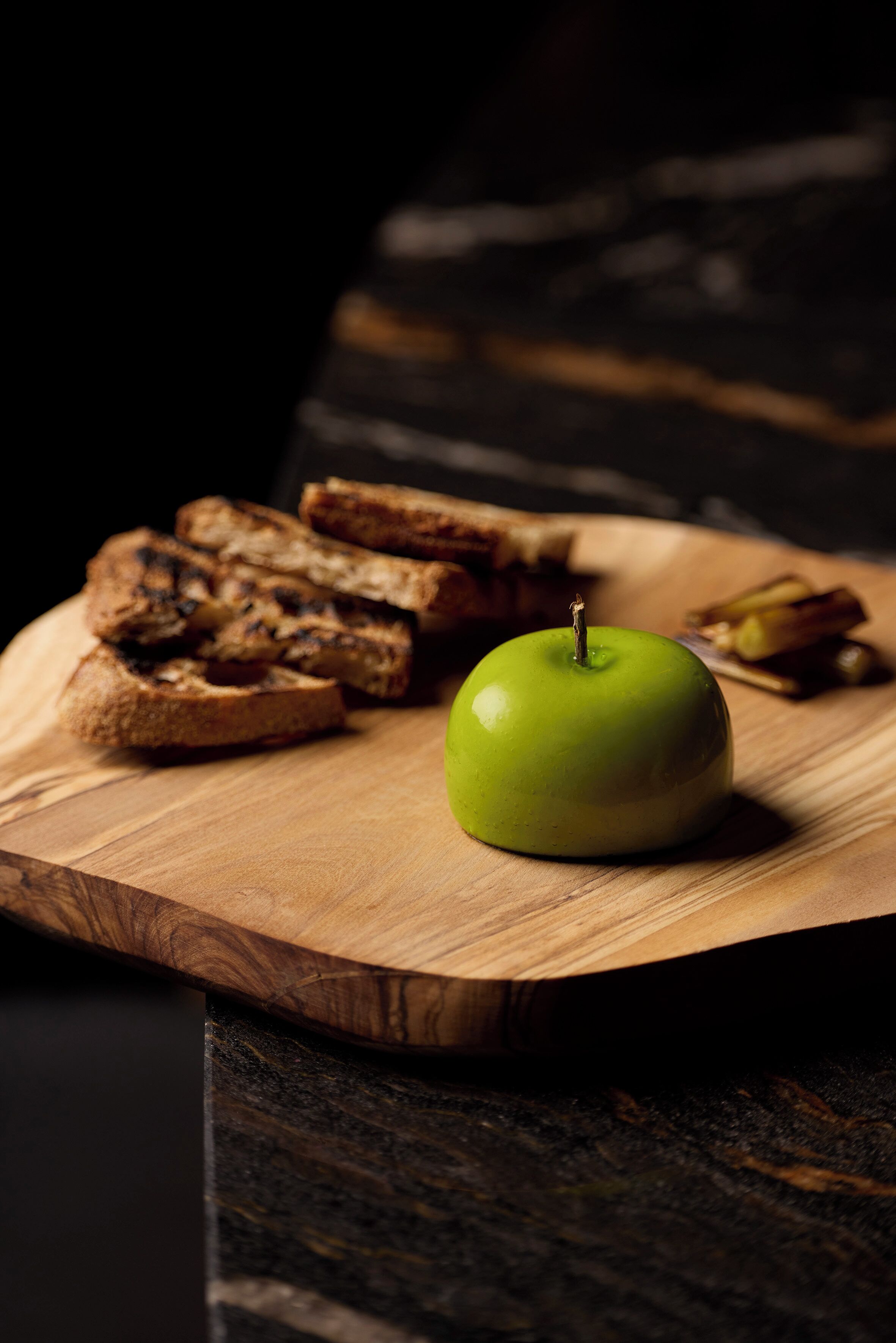 Una tabla de madera con tostadas y una manzana verde.