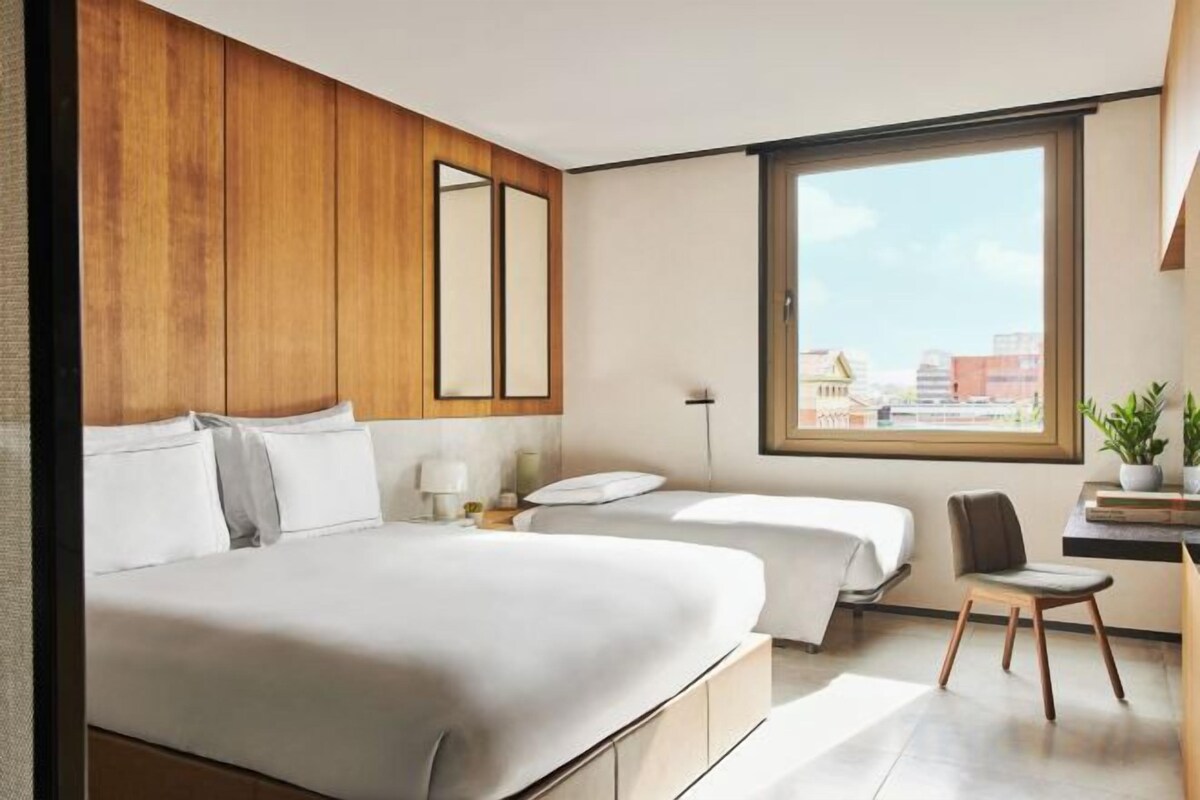 A modern hotel room with a large bed, a desk, and a view of the city.